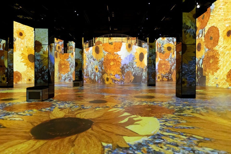 Room with large digital projections of sunflowers covering the walls and floor in an immersive art installation.