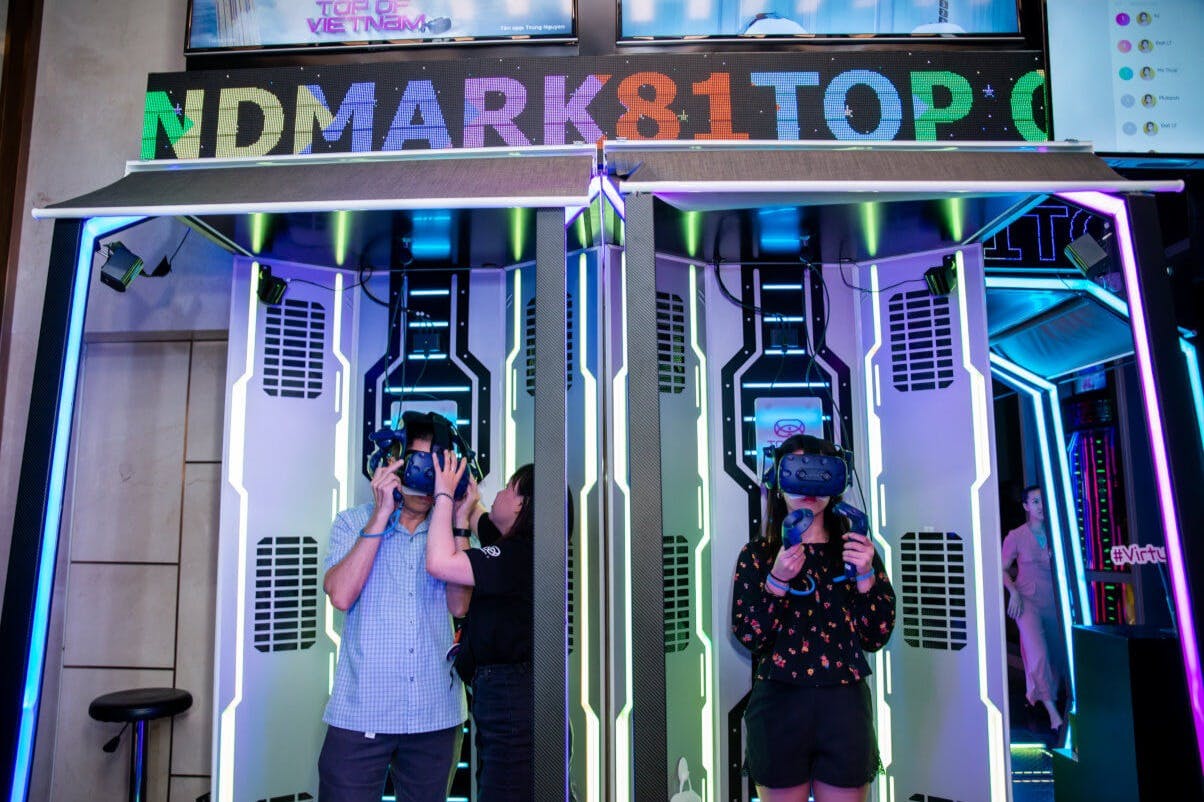 Two people wearing VR headsets inside a colorful VR booth with the sign "LANDMARK81TOP" above them.