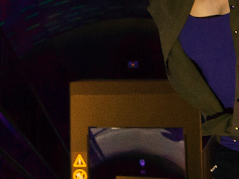 Two people, one crouching and one standing, inside a tunnel with vibrant purple and blue lighting and mesh sides.