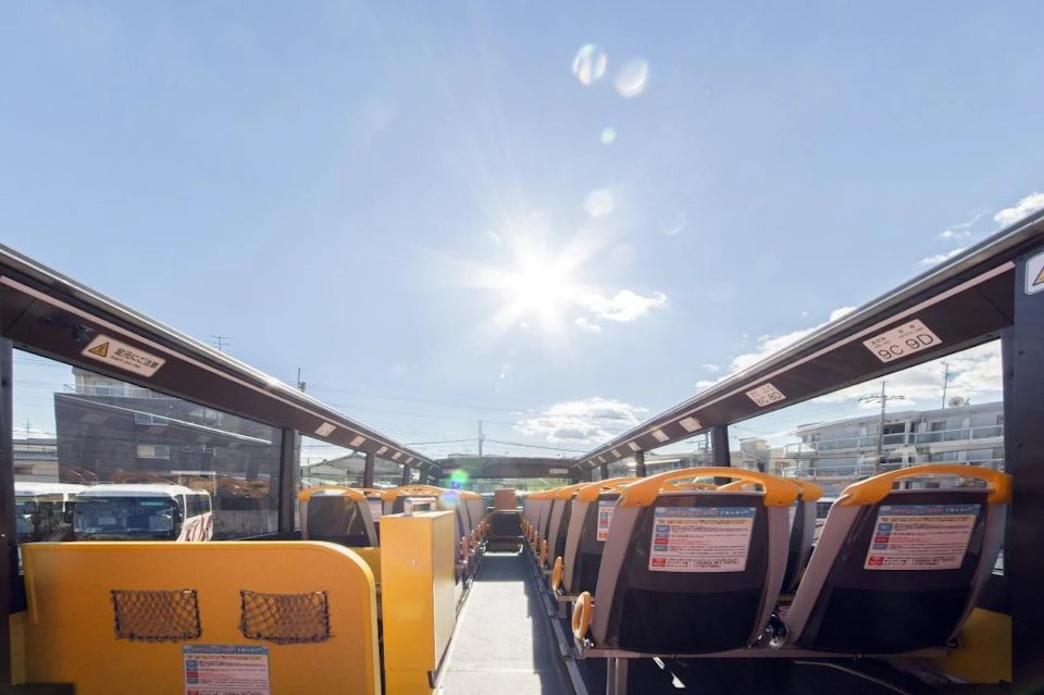 Interior of an open-top bus with yellow and black seats under a clear sunny sky.