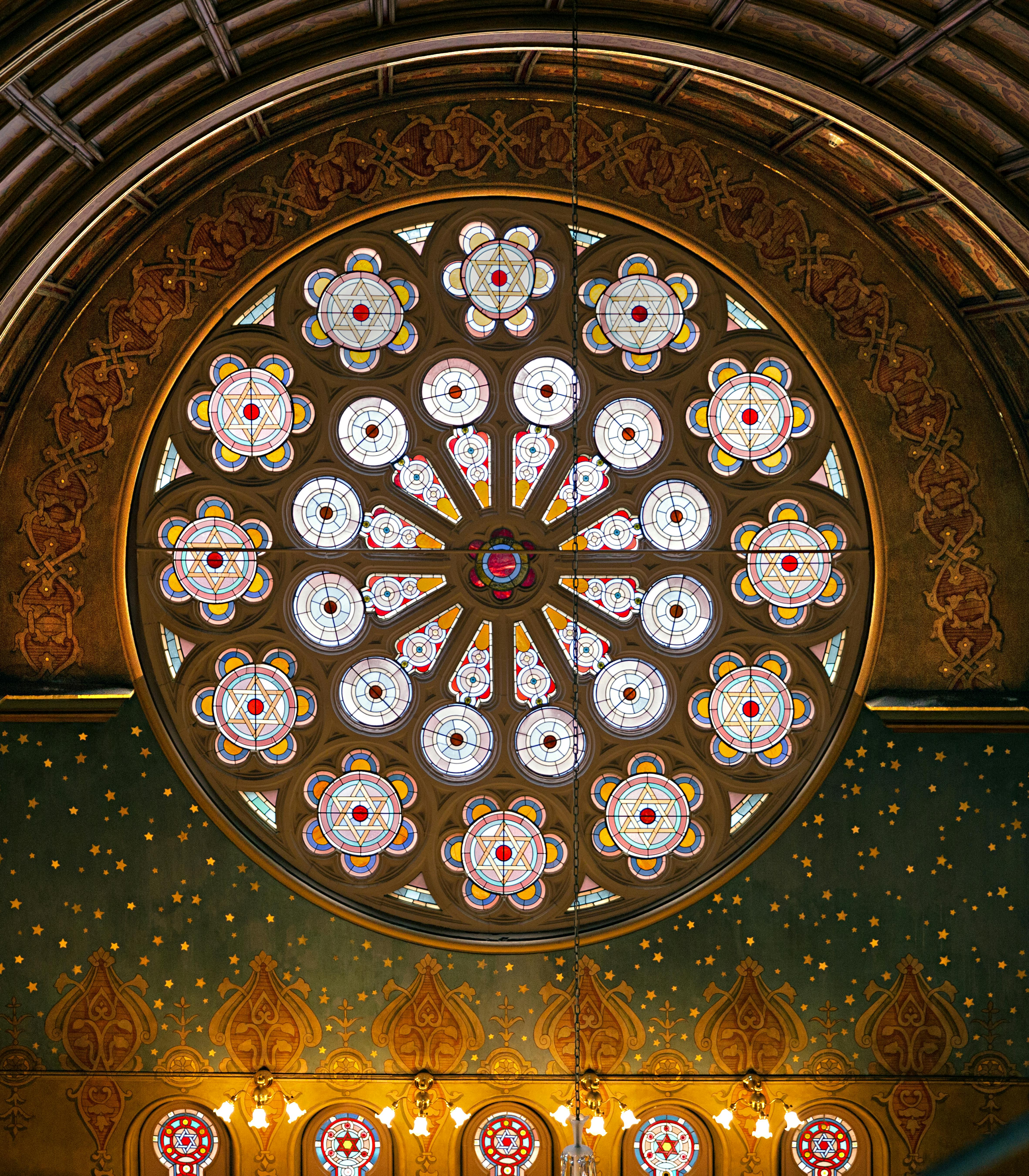 Vitrail circulaire présentant des motifs floraux complexes aux couleurs éclatantes, placé dans un mur ornementé.