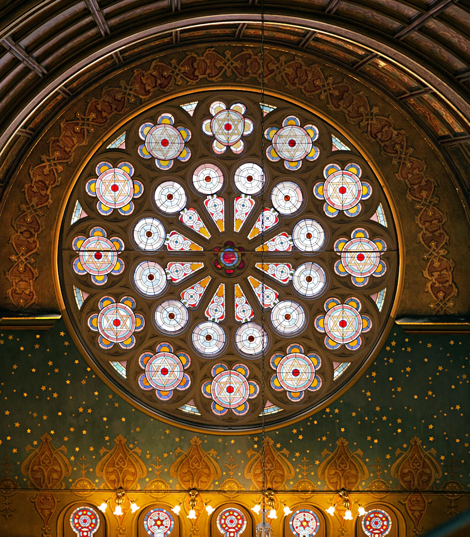 A circular stained glass window featuring intricate floral patterns with vibrant colors, set in an ornately decorated wall.