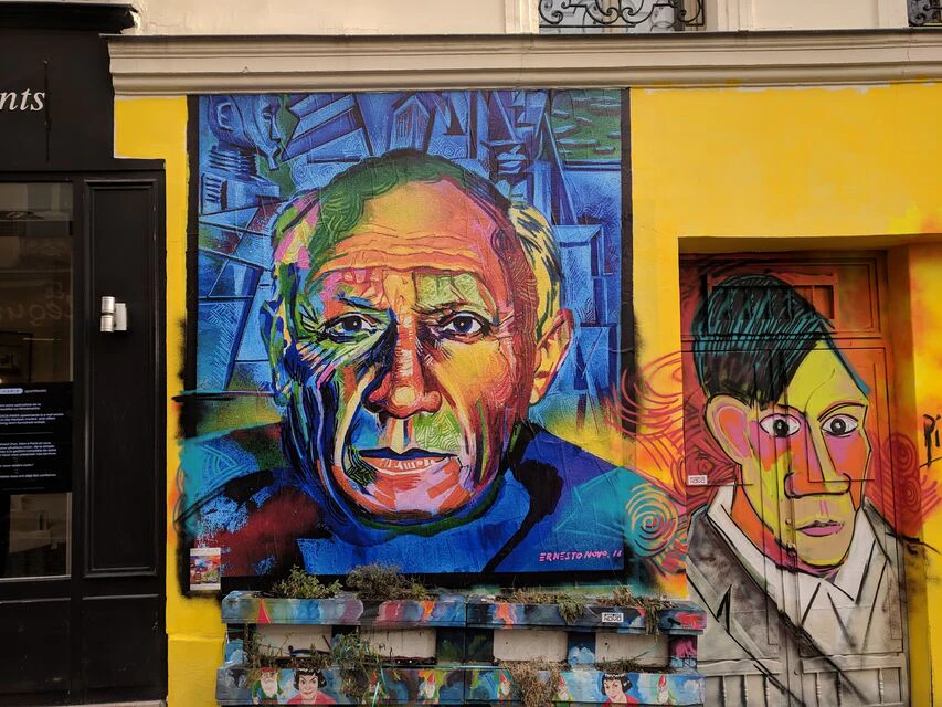 Colorful mural of an older man's face on a yellow wall, with vibrant, abstract background elements and a small window to the right.