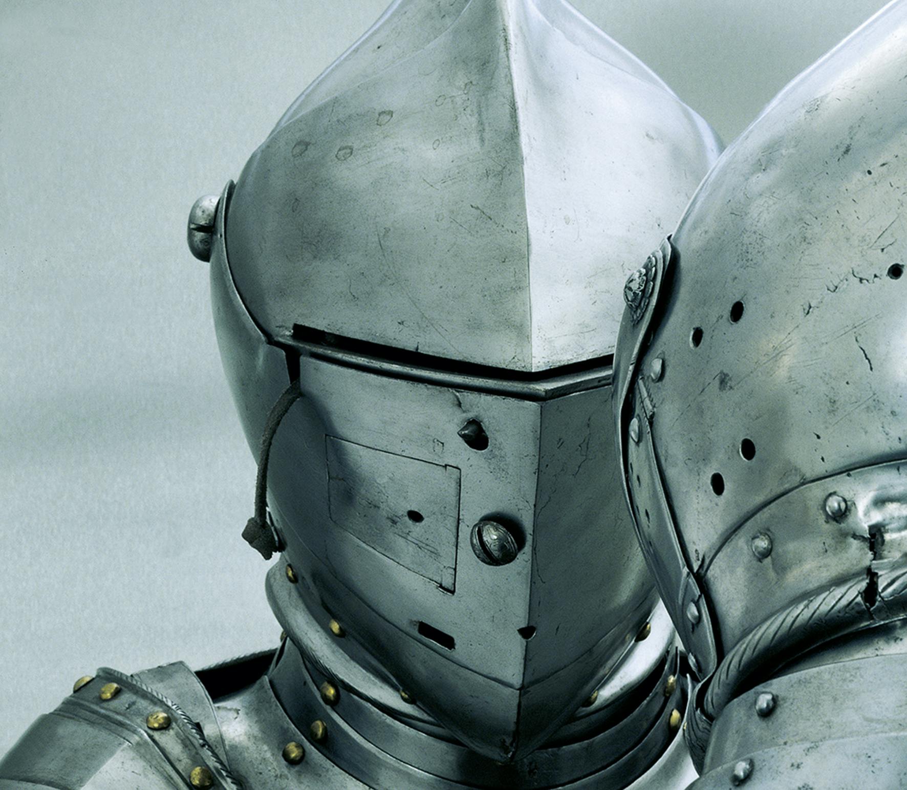 Close-up of two suits of medieval knight armor, featuring metal helmets with narrow eye slits and riveted joints.