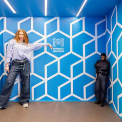 Två personer i ett blått rum med geometriska mönster, varav en verkar större på grund av en optisk illusion på Illusionsmuseet.