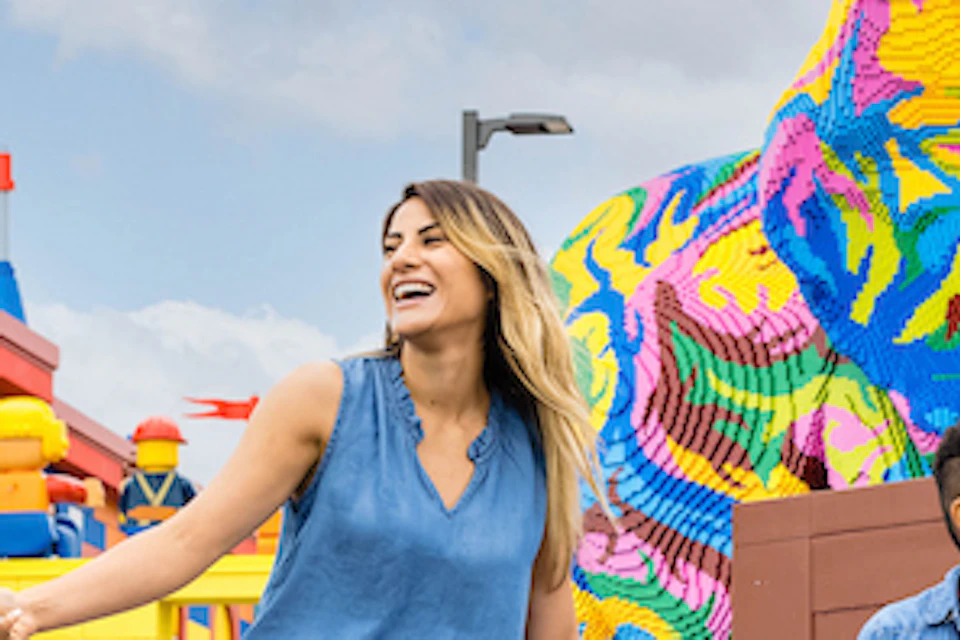 A family of four poses with Lego characters in front of the entrance to LEGOLAND New York, featuring colorful Lego structures.