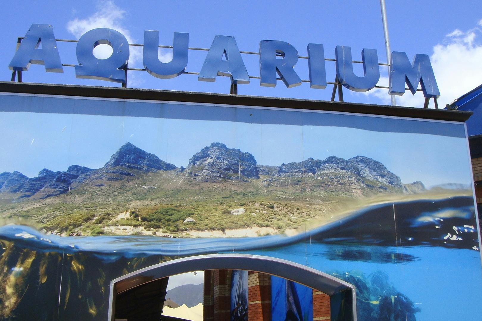 A sign reading "Aquarium" with a scenic mountain and underwater theme design under a clear blue sky.