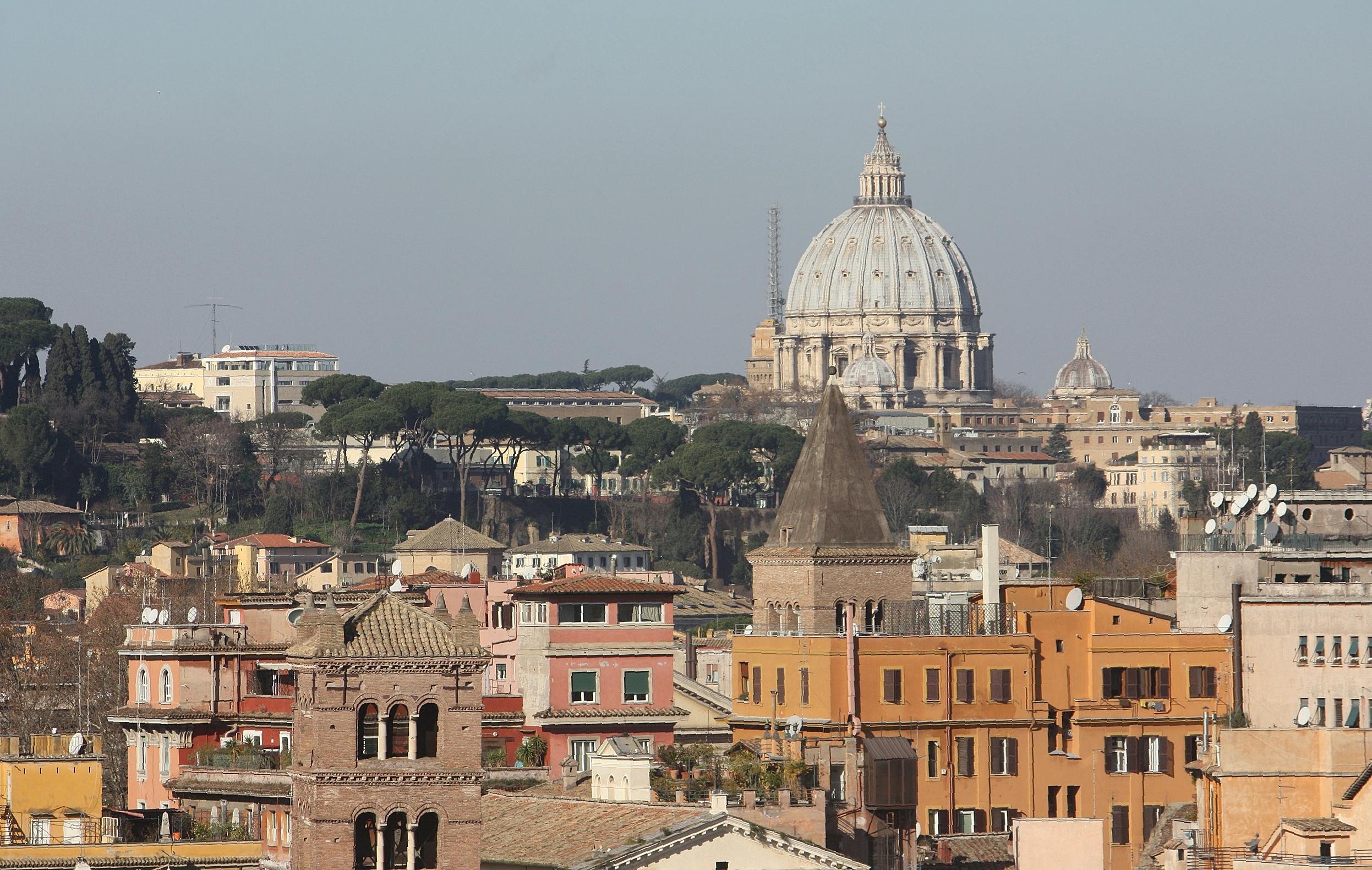 Vue du dôme de la basilique Saint-Pierre entouré de bâtiments urbains, dont des clochers et des maisons colorées, à Rome.
