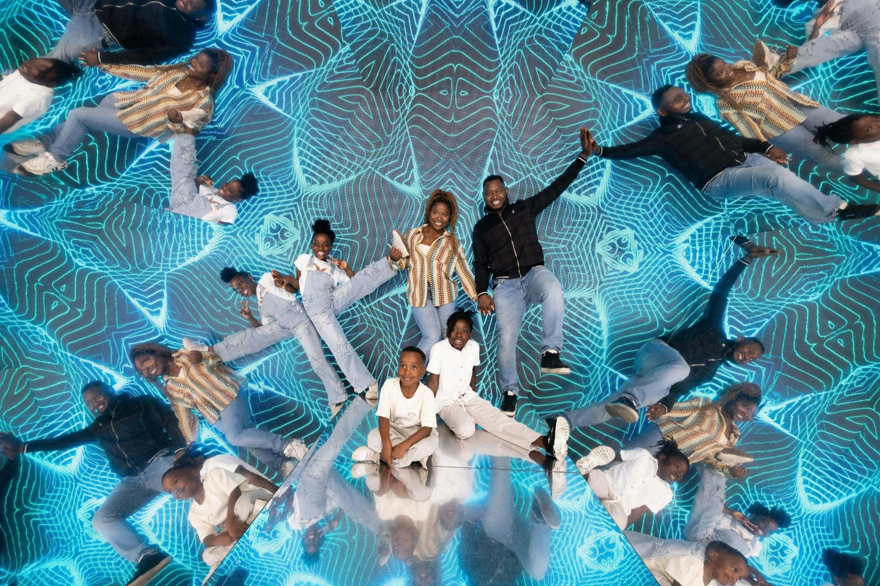 En grupp människor som poserar i ett speglat rum med blåmönstrad belysning som skapar en kalejdoskopisk effekt.