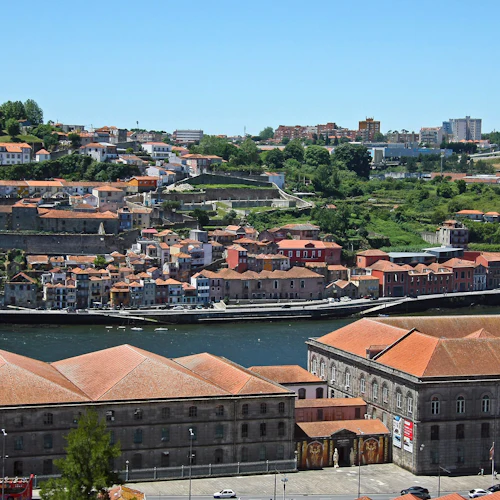 En stadsbild vid floden med en blandning av gamla och nya byggnader på en sluttning, under en klarblå himmel.