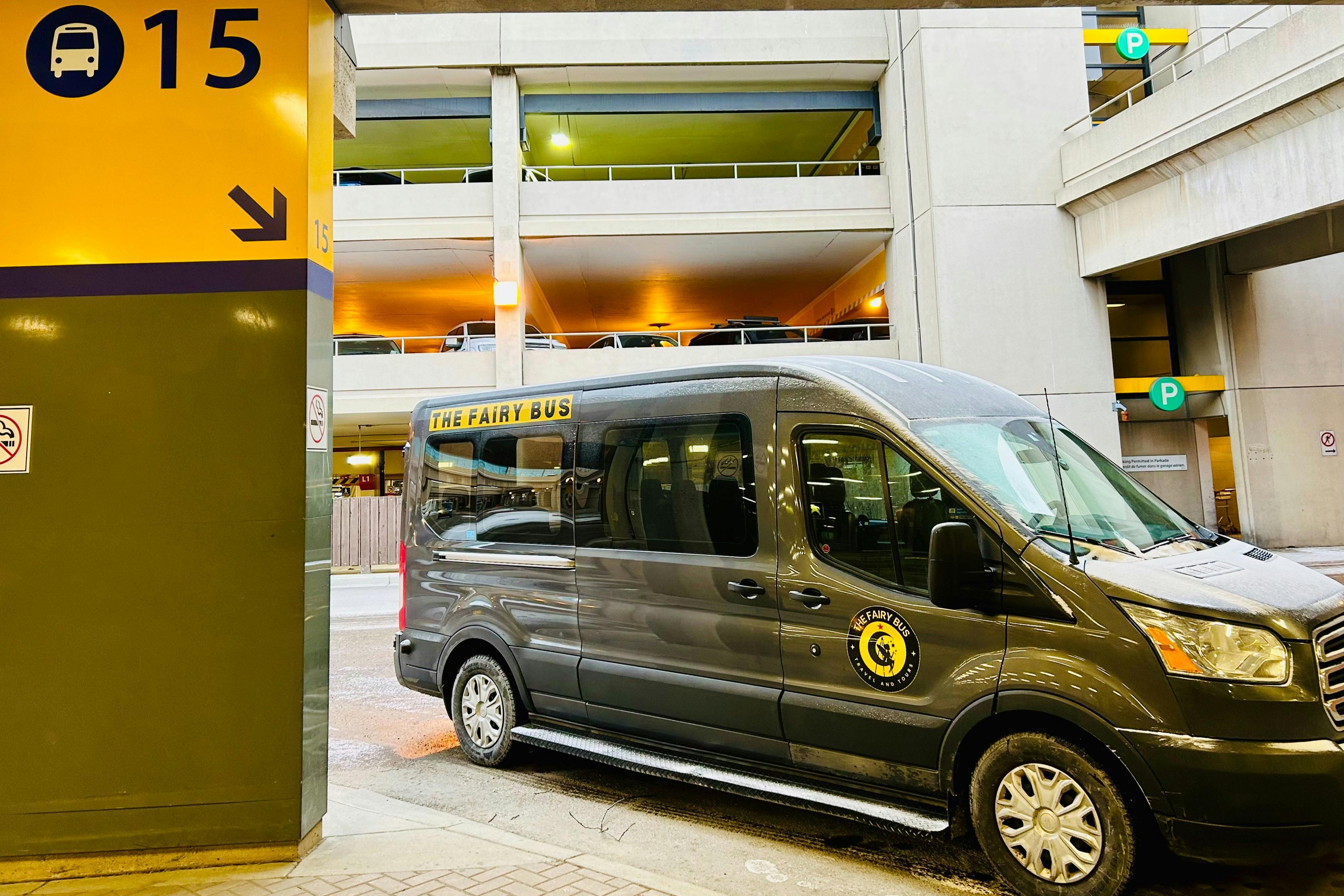 A gray van labeled "The Fairy Bus" is parked near a multi-story parking garage, with signs and lighting visible in the background.