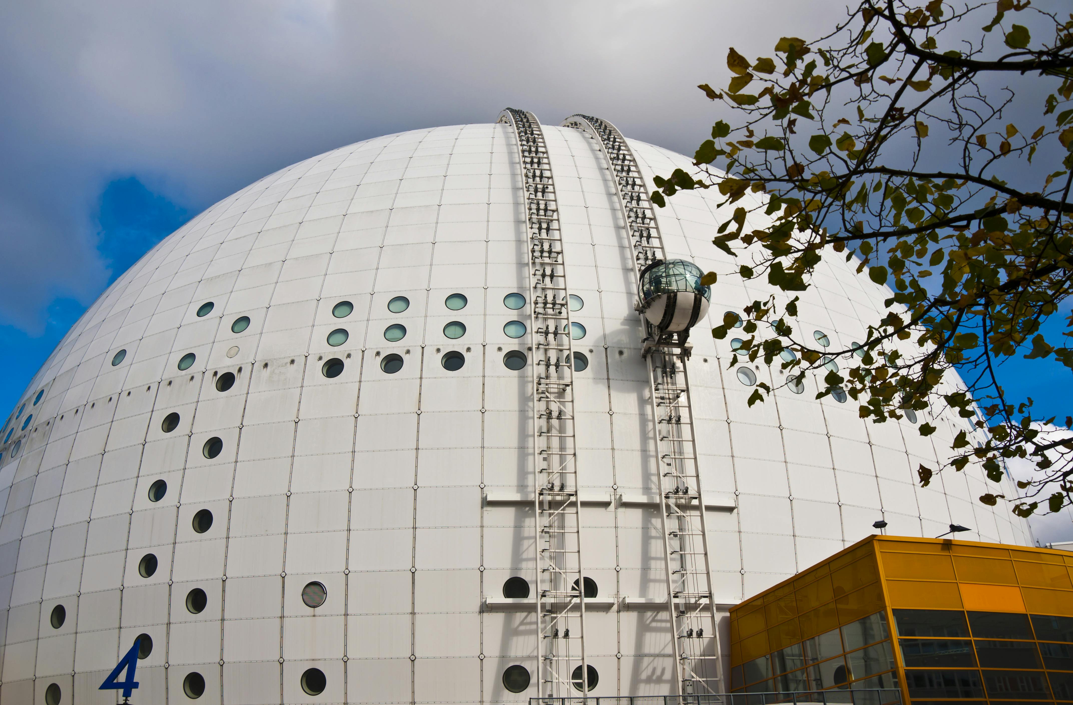 Large, white dome structure with circular windows and a glass gondola on tracks. A tree branch is visible in the foreground.