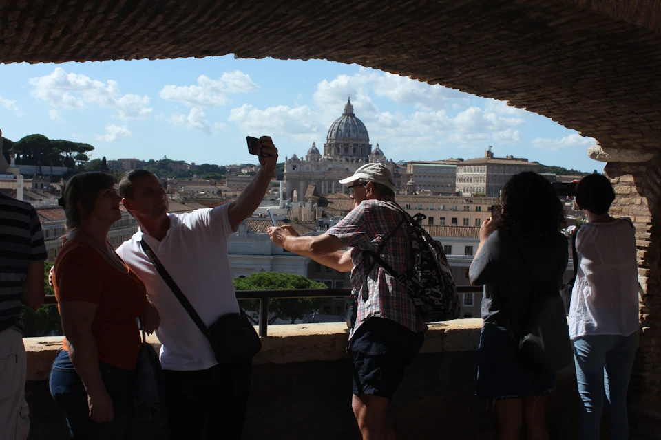 Several people taking photos from a terrace with a view of a cityscape, featuring a prominent dome structure in the background.