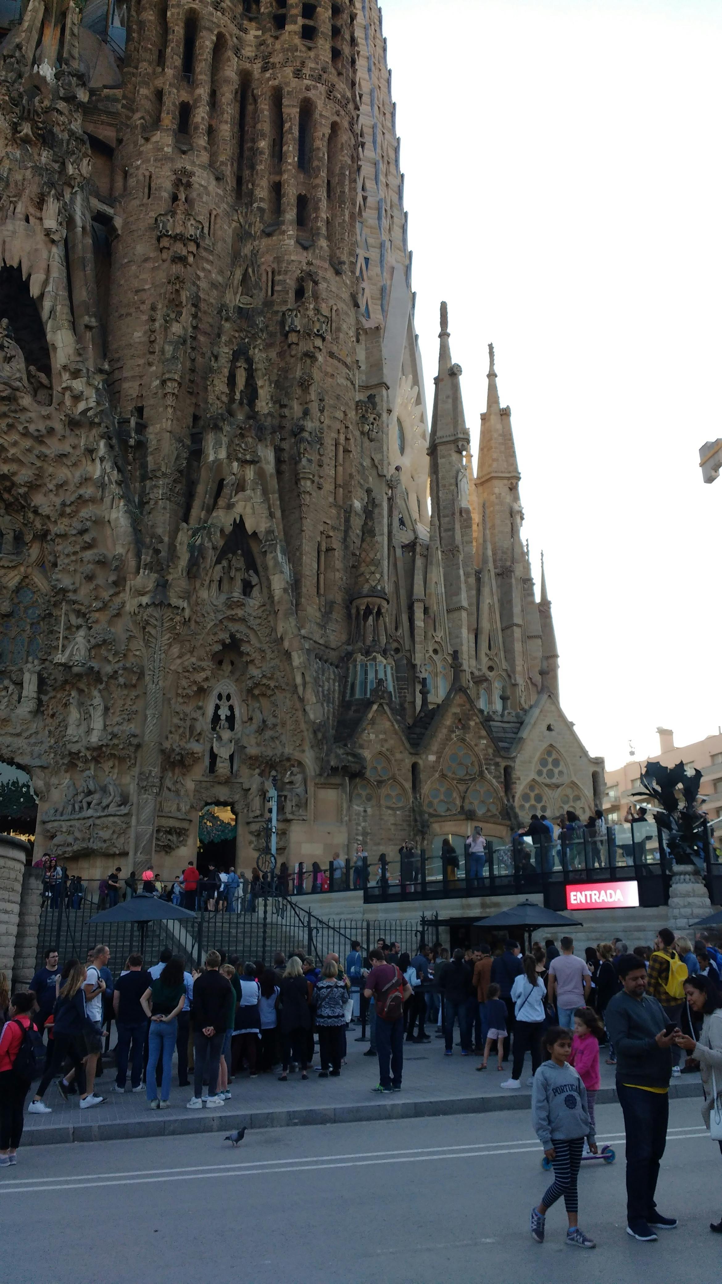 People gathered at the entrance of Sagrada Família, a large, ornate cathedral with intricate sculptures and spires.