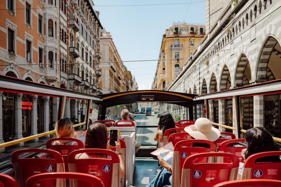 Passengers seated on an open-top tour bus traveling through a city with historic buildings under a clear sky.