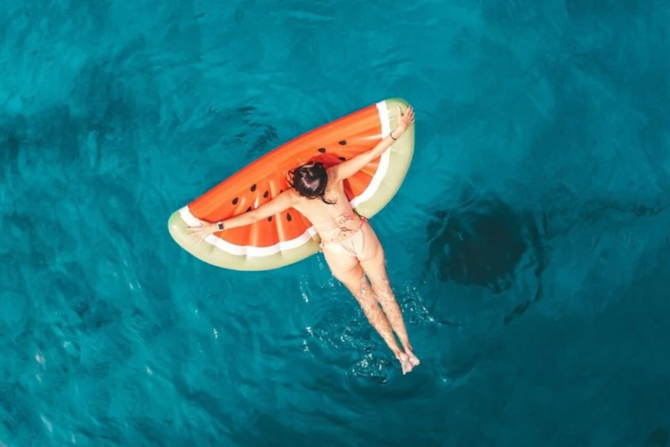 A person floating on a watermelon-shaped inflatable in a body of water, viewed from above.