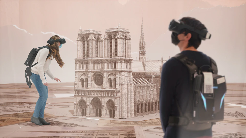 Two people wearing virtual reality headsets interact with a digital model of Notre Dame Cathedral in a room.