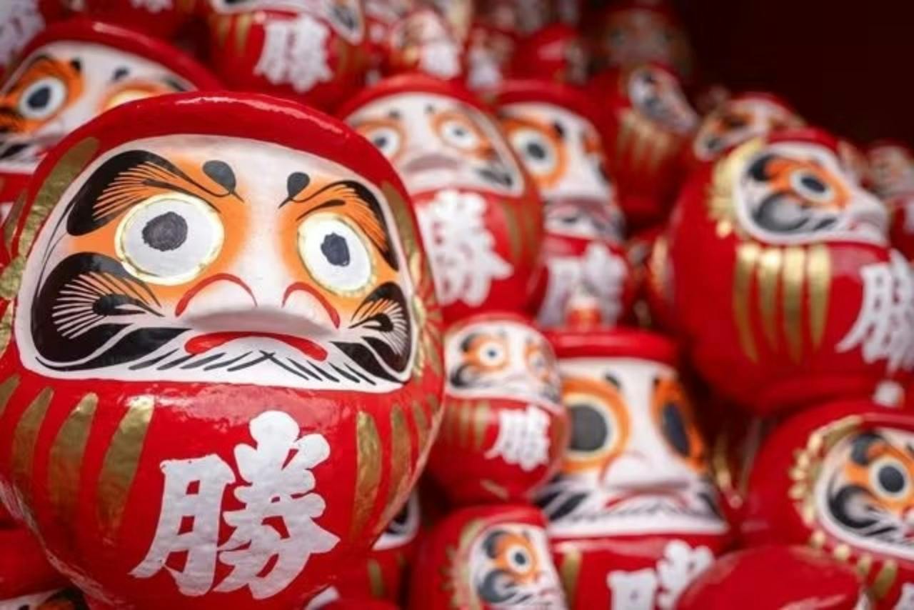 A collection of red Daruma dolls with painted faces and Japanese characters, arranged closely together.