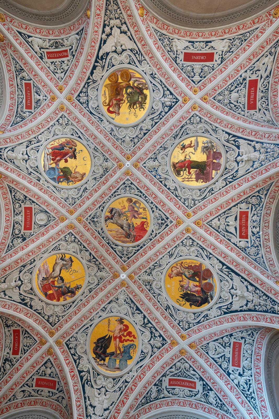 Soffitto ornato con motivi intricati e sei affreschi circolari che raffigurano varie scene mitologiche. Testo latino in pannelli rossi.