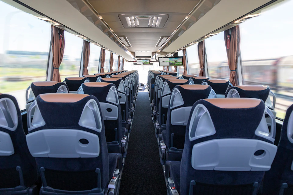 Interior view of a modern coach bus with rows of empty seats and mounted screens visible at the front.