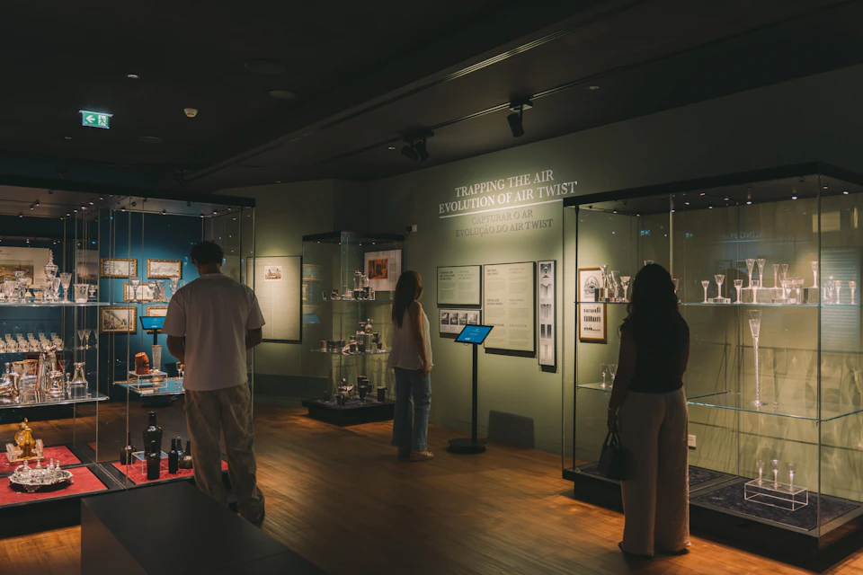 People viewing glass displays and informational panels in a dimly lit museum exhibit.