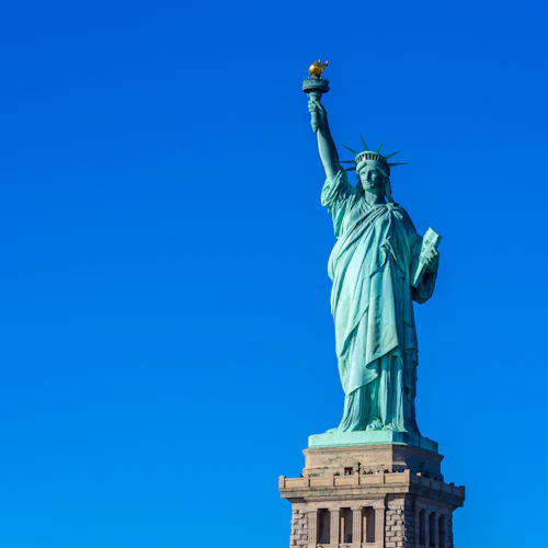 Die Freiheitsstatue, die eine Fackel und eine Tafel in der Hand hält, steht vor einem strahlend blauen Himmel.