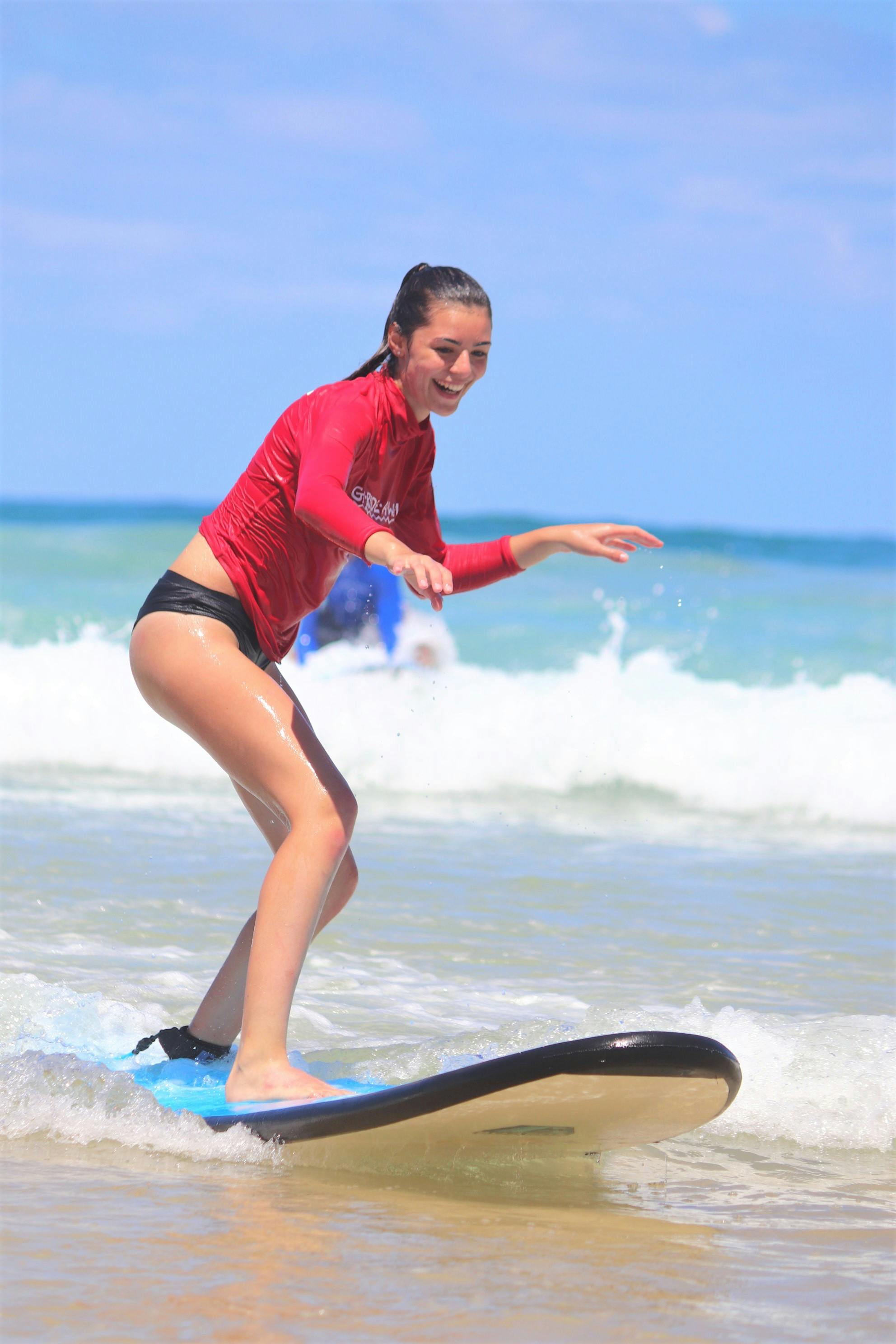 파도와 푸른 하늘을 배경으로 바다에서 서핑을 즐기거나 균형을 잡는 검은 수영복과 붉은 발진 가드를 입은 사람.