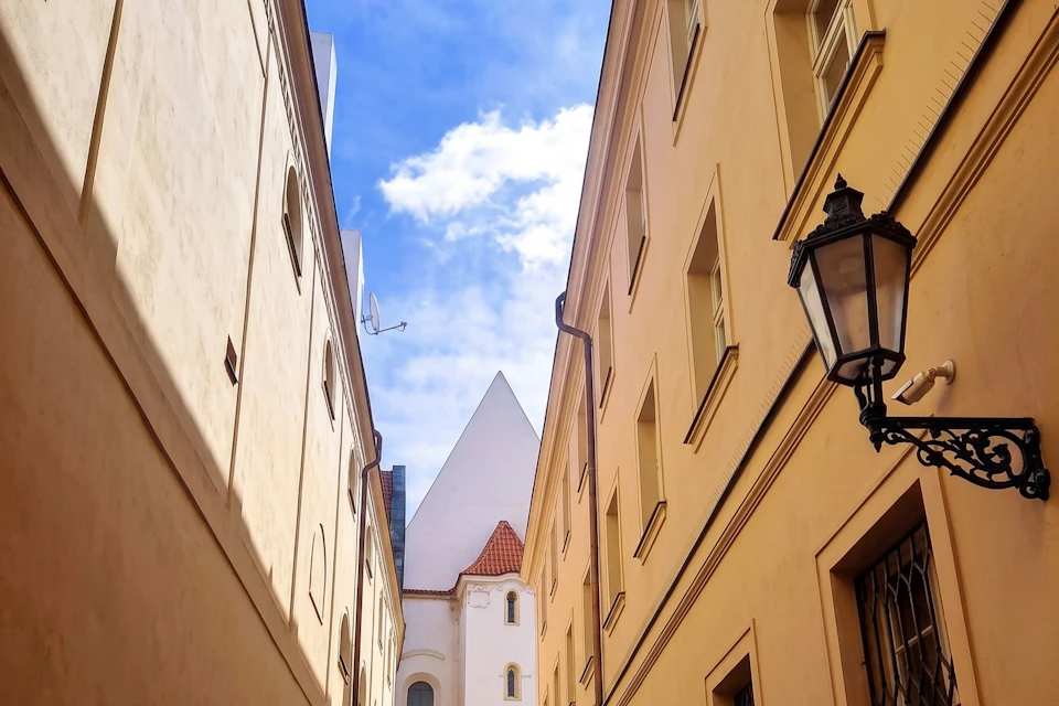 A narrow street between light-colored buildings, leading to a white church with a triangular roof under a blue sky.