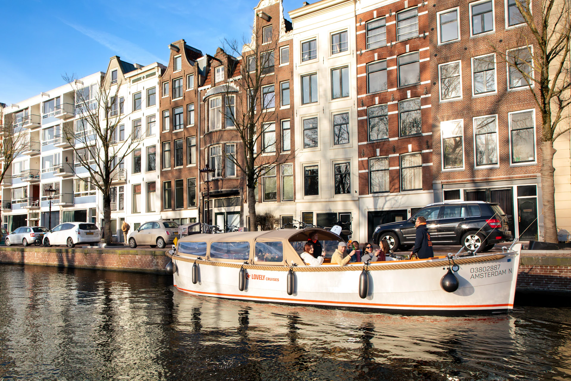 A boat with passengers cruises along a canal in front of classic European townhouses under a clear blue sky.