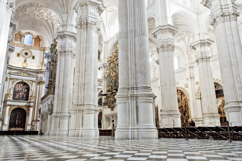 Interior of a grand cathedral with tall white columns, ornate gold details, and checkered floor tiles.