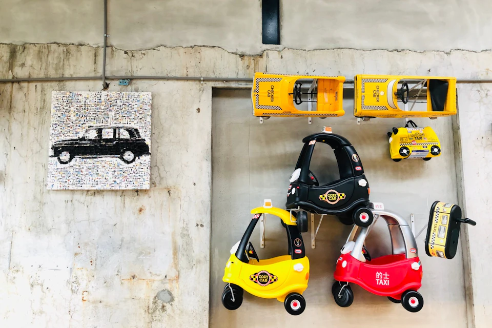 Toy cars, including yellow and black taxis, are mounted on a wall with a painted black car artwork in the background.