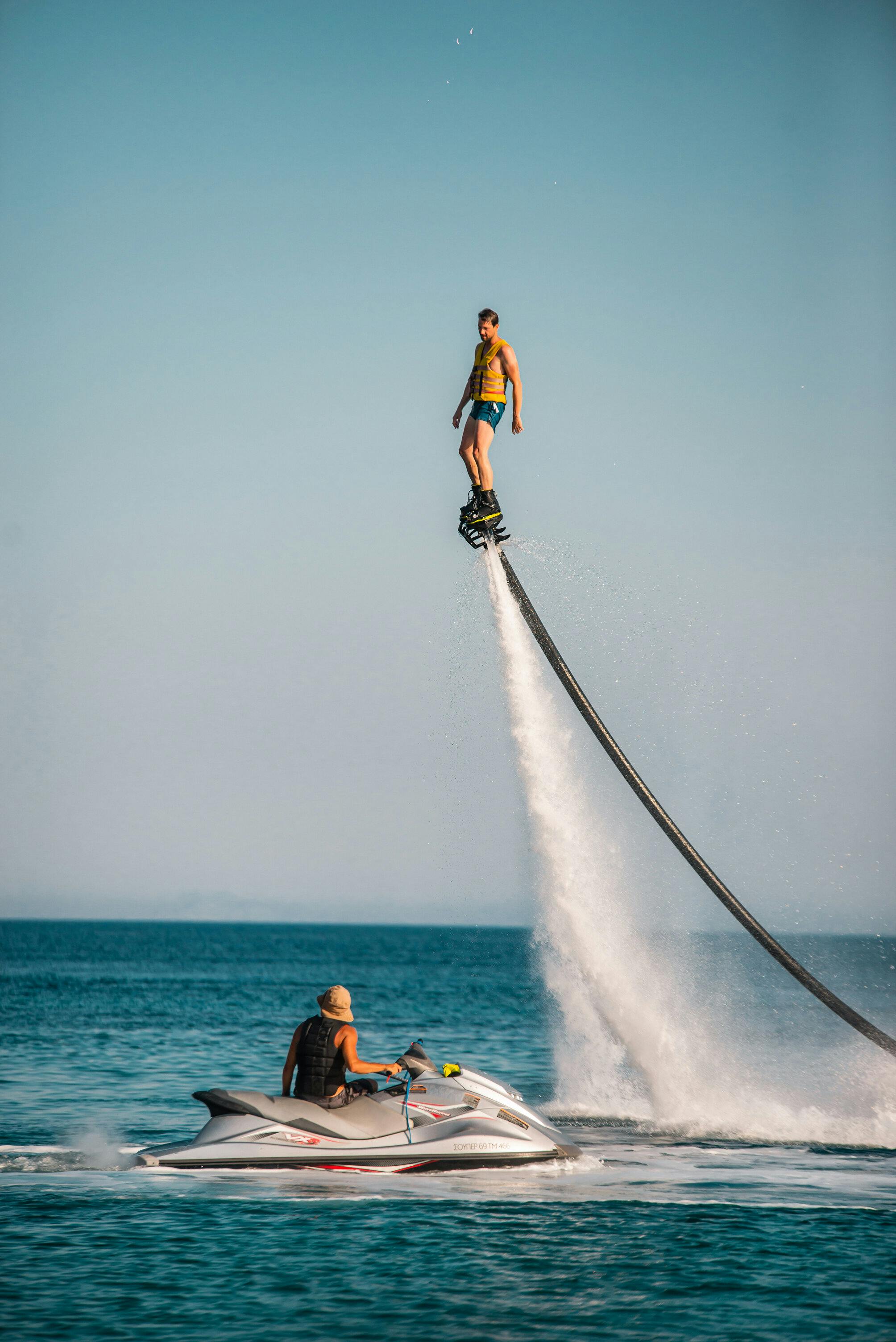 워터젯으로 바다 위를 날아다니는 사람, 맑은 하늘 아래 근처에서 제트 스키를 운영하는 사람.