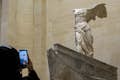 Eine Person, die mit ihrem Handy im Louvre-Museum ein Foto der Skulptur Nike von Samothrake macht
