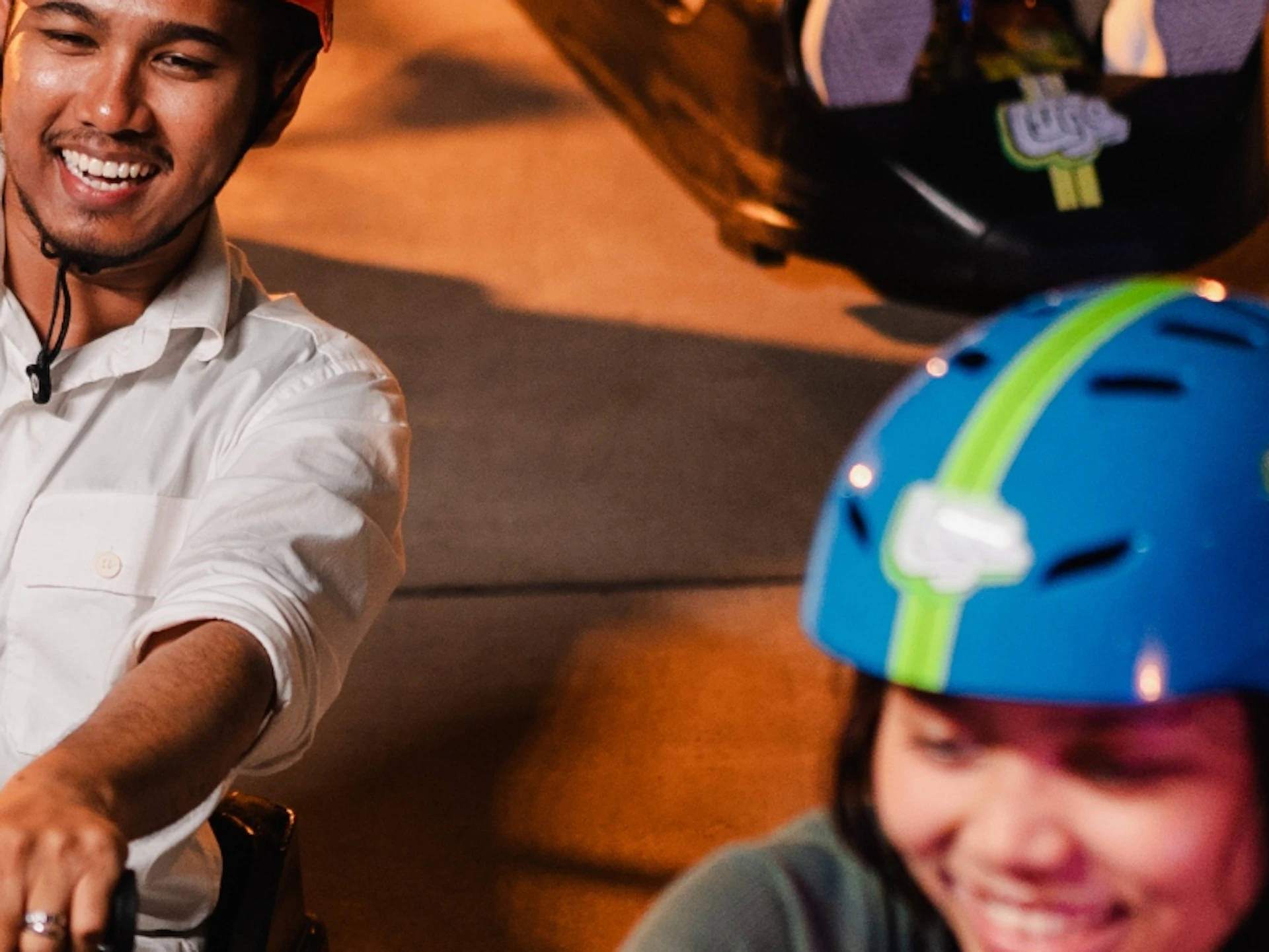 A group of people riding luges on a lit pathway, wearing helmets and smiling.