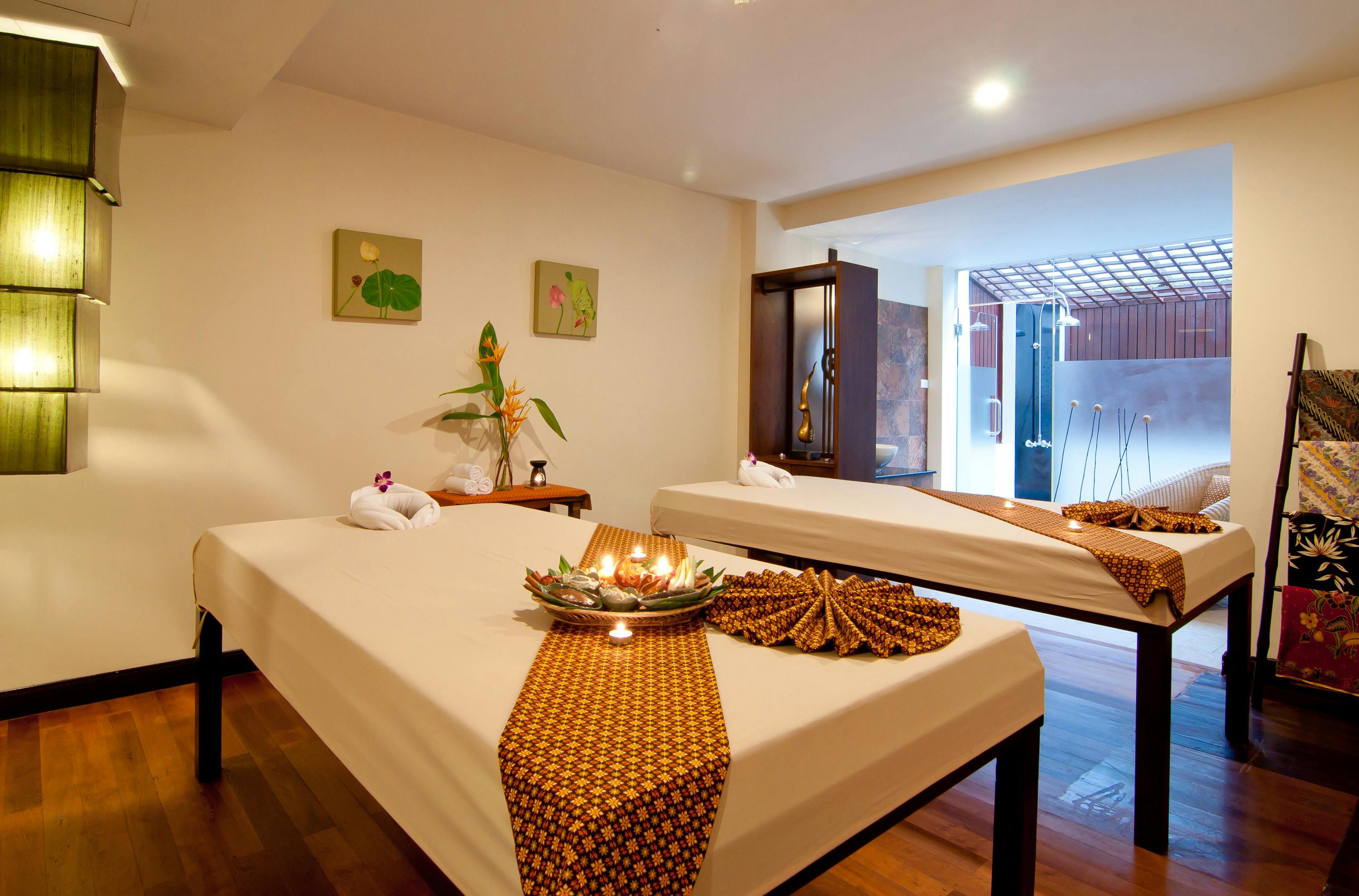 Przytulna sala spa z dwoma stolikami do masażu, świecami i elementami dekoracyjnymi, charakteryzująca się ciepłą i relaksującą atmosferą.