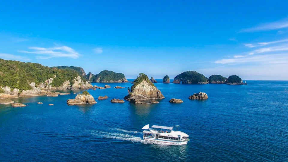 A white boat cruises through a blue sea dotted with small rocky islands under a clear blue sky.
