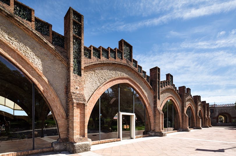 Une rangée de portes arquées en briques avec des portes et des fenêtres en verre, reflétant les arbres et le ciel, sous un ciel bleu avec des nuages.