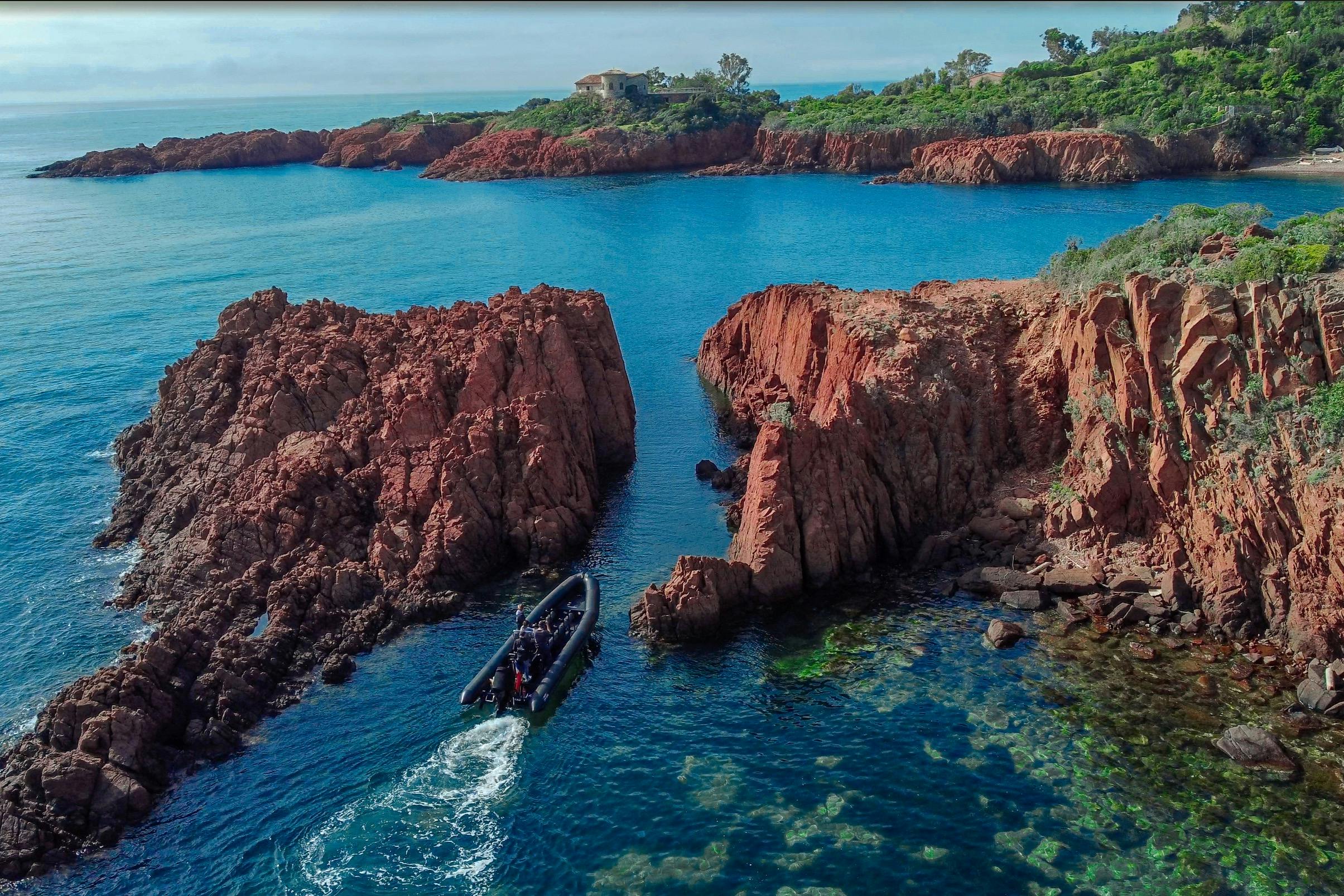 一艘小船在蓝色大海上的红色岩石之间航行，背景是远处的海岸线和绿色植物。