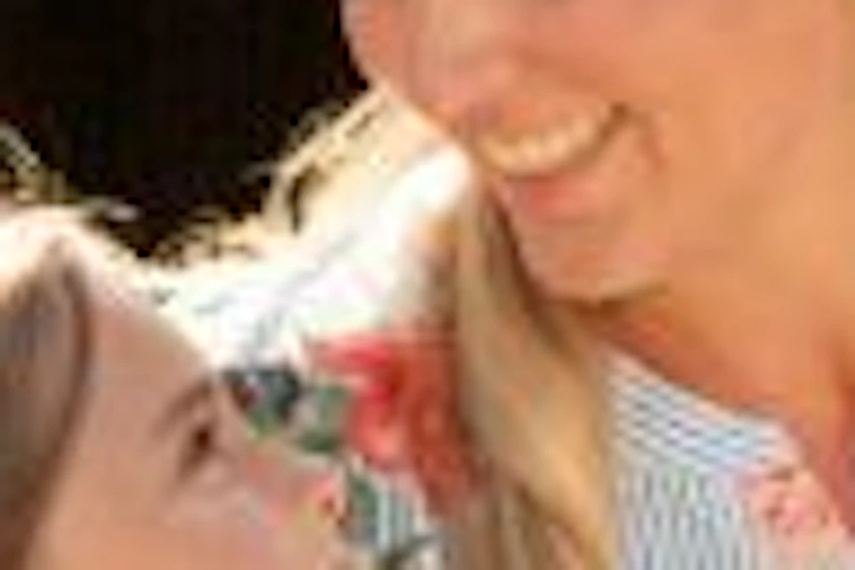 A woman and a young girl smiling at each other while riding an elephant-themed amusement park ride.