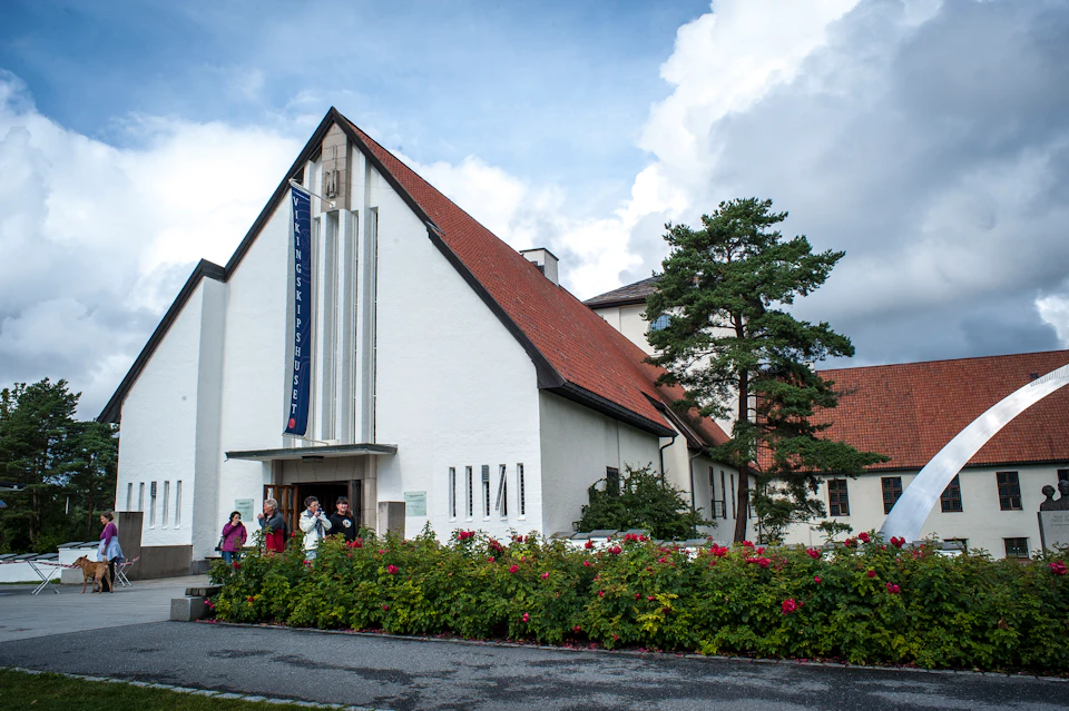 White church-like building with a red roof, a "Vigelandmuseet" banner, surrounded by greenery and several people at the entrance.