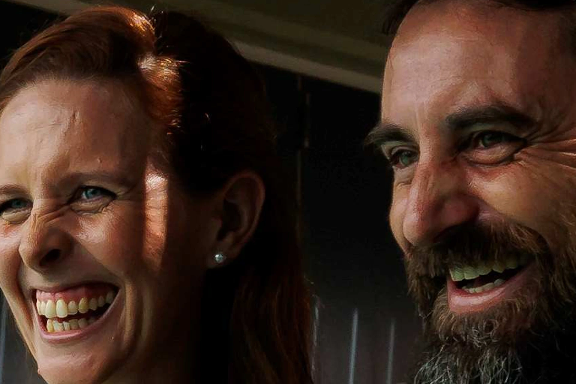 Two people laughing while looking at an aquarium exhibit, standing in a dimly lit room.