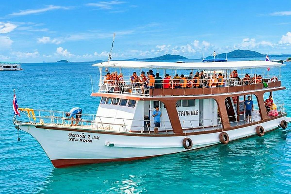 A white boat named "Sea Born" with people on board floating on clear blue water, with distant islands in the background.