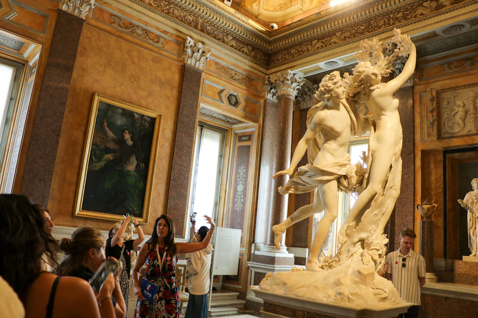 Visitors in an ornate museum room with artwork on the walls and a sculpture in the foreground.