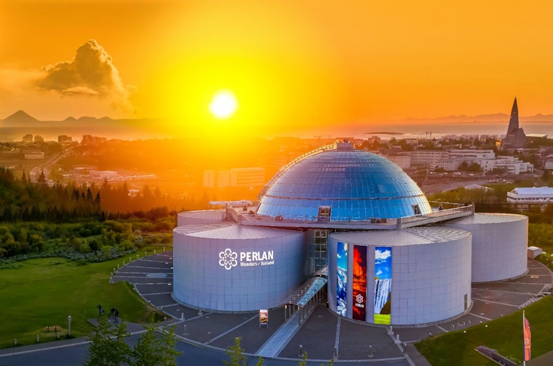 活気に満ちたオレンジ色の夕日の下、街の景色を背景に「ペルランアイスランドの不思議」とラベル付けされた未来的なガラスドームの建物。