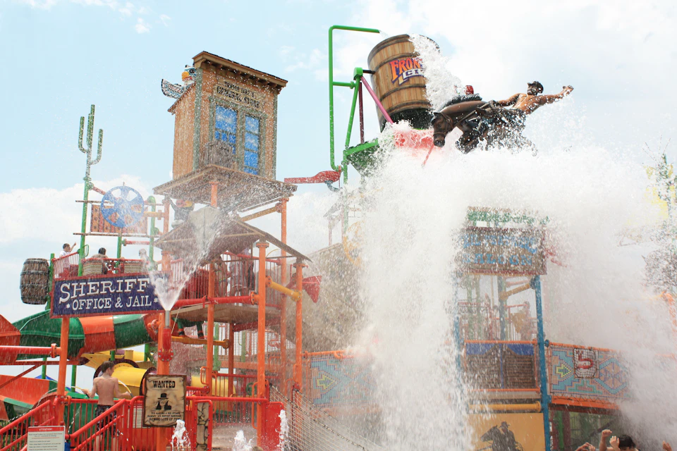A water park play area with colorful structures and a large bucket splashing water onto the ground.