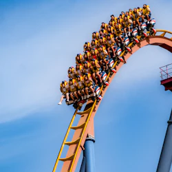 Människor som åker berg- och dalbana, med en grupp passagerare som går nerför en brant slinga under en klarblå himmel.