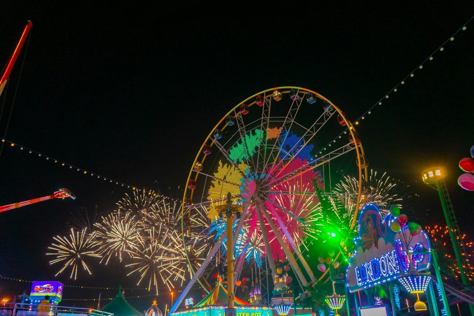 밤하늘을 밝히는 화려한 조명과 불꽃놀이가 있는 박람회장의 활기찬 관람차.