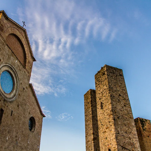 Stenkyrkans fasad med cirkulärt glasmålningsfönster och intilliggande fyrkantiga torn under en blå himmel med blöta moln.