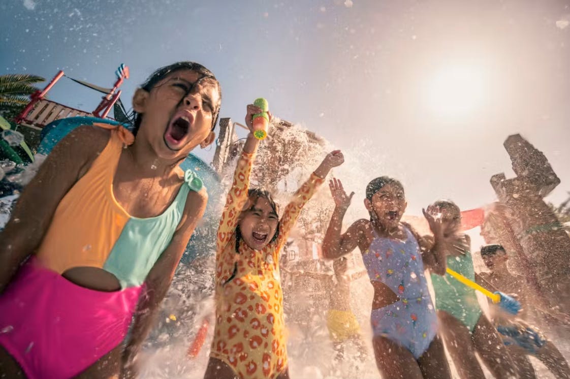 Bambini in costumi da bagno coloratissimi che giocano allegri sotto i getti d'acqua in un parco acquatico in una giornata di sole.