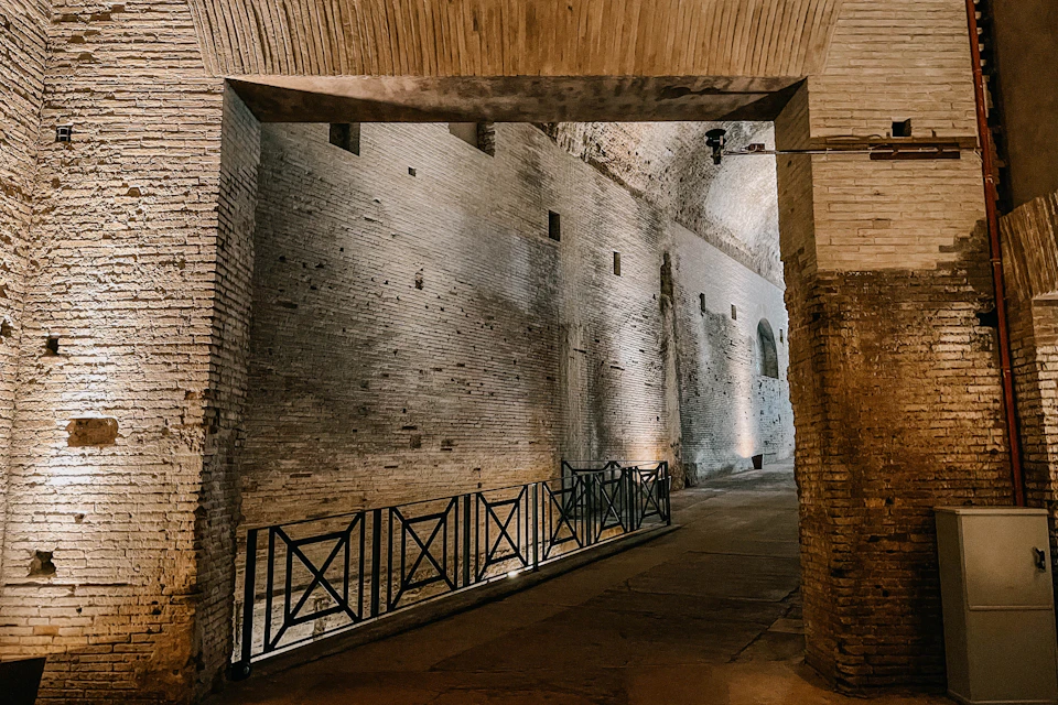 Stone interior of an ancient structure with illuminated walls, an arched ceiling, and a metal railing along a pathway.